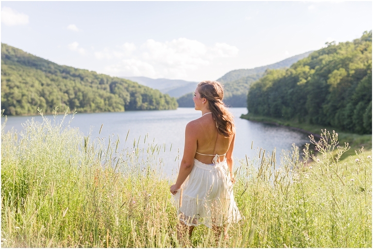 Senior photos of a girl in a white dress in a field by the lake with a mountain view