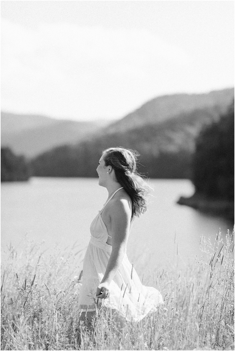 Senior photos of a girl in a white dress in a field by the lake with a mountain view taken by a Virginia graduation photographer