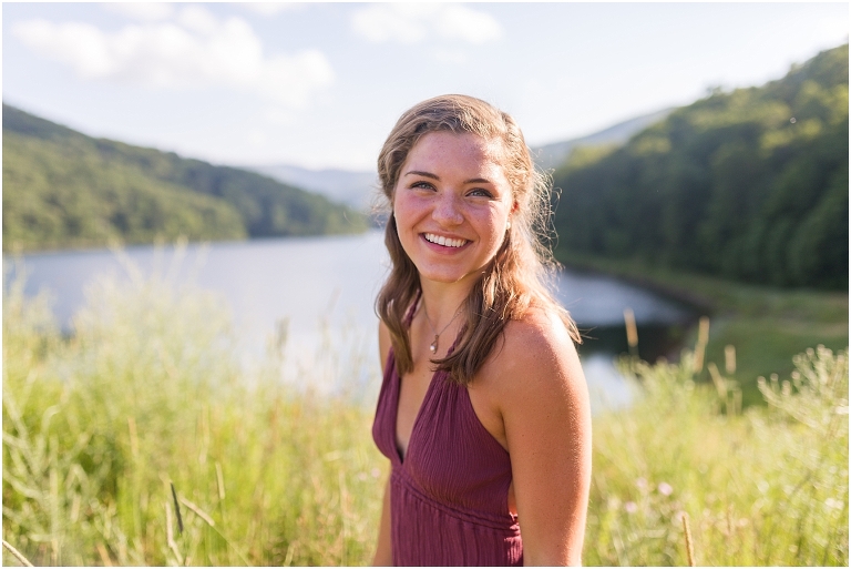Senior photos of a girl in a purple dress in a field overlooking a lake with a mountain background taken by a Virginia portrait photographer