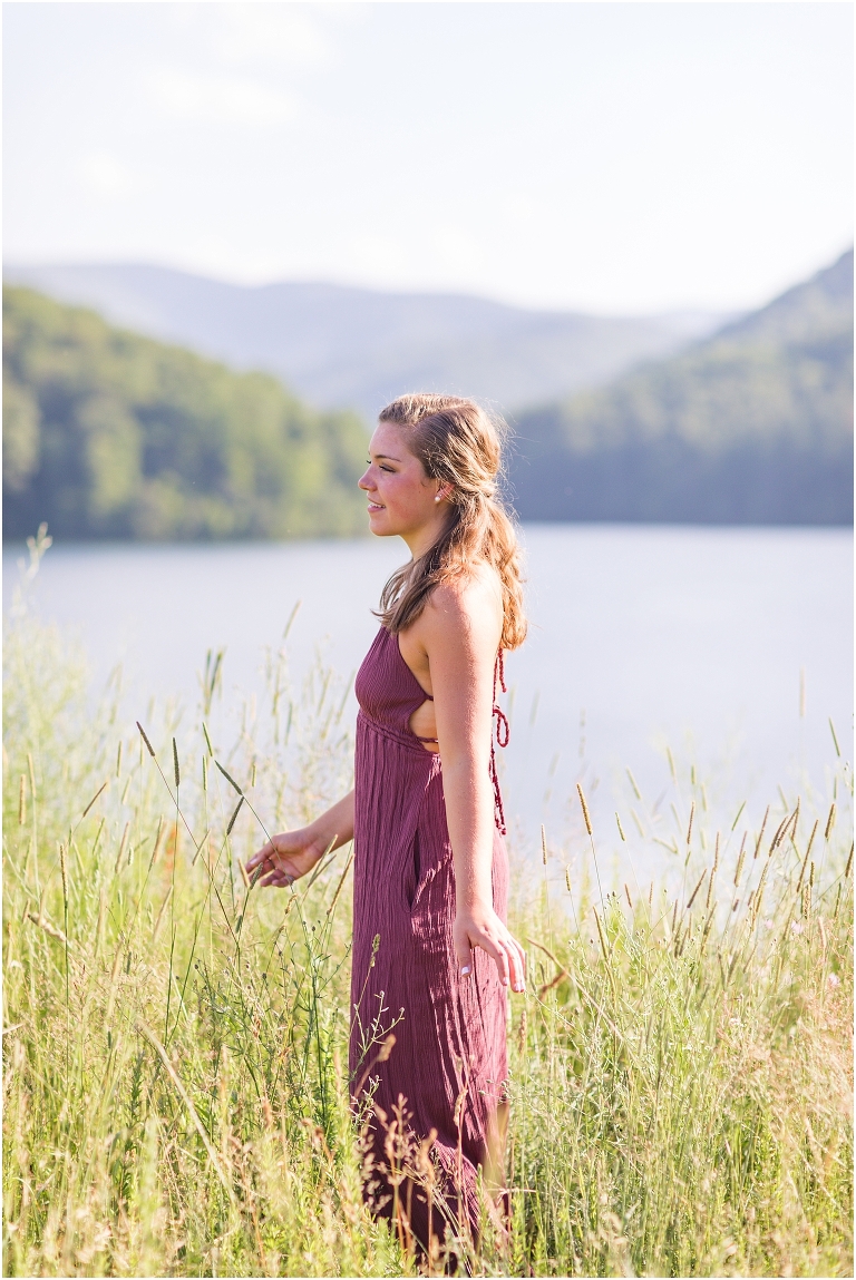 Senior photos of a girl in a purple dress in a field overlooking a lake with a mountain background taken by a Virginia portrait photographer