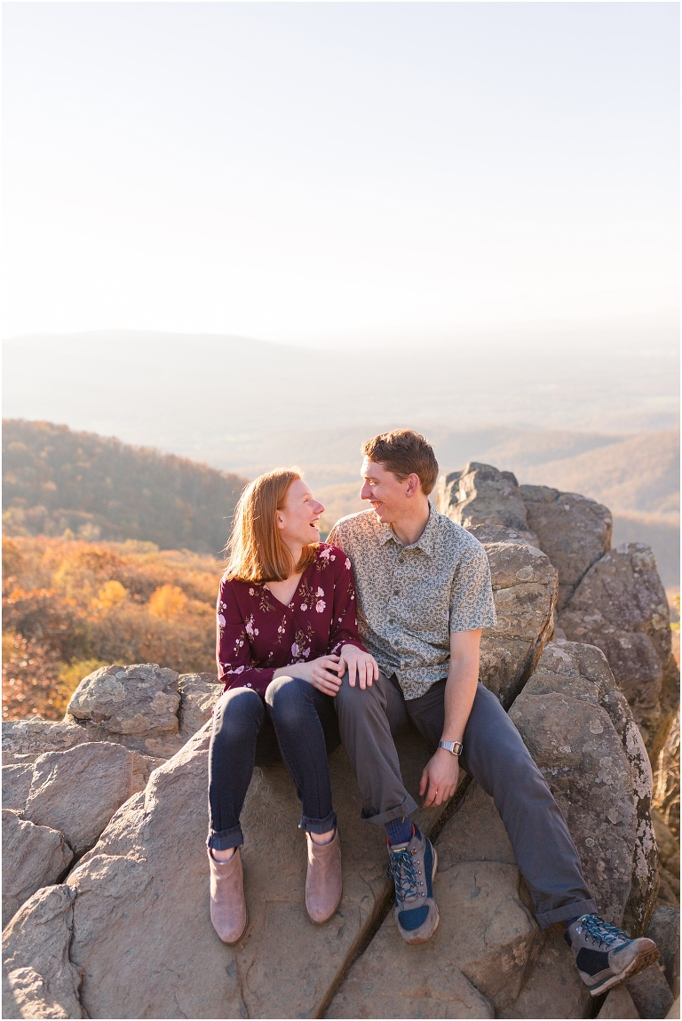 Couple sits together at Humpback Rocks during sunset, surrounded by fall colors and blue sky.