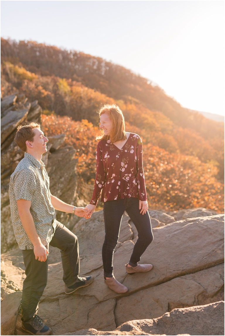 Couple sits together at Humpback Rocks during sunset, surrounded by fall colors and blue sky.