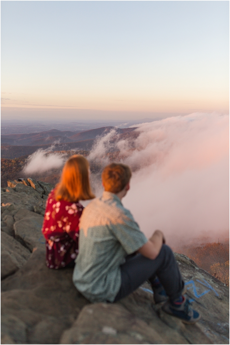 Couple sits together at Humpback Rocks during sunset, surrounded by fall colors and mountain fog.