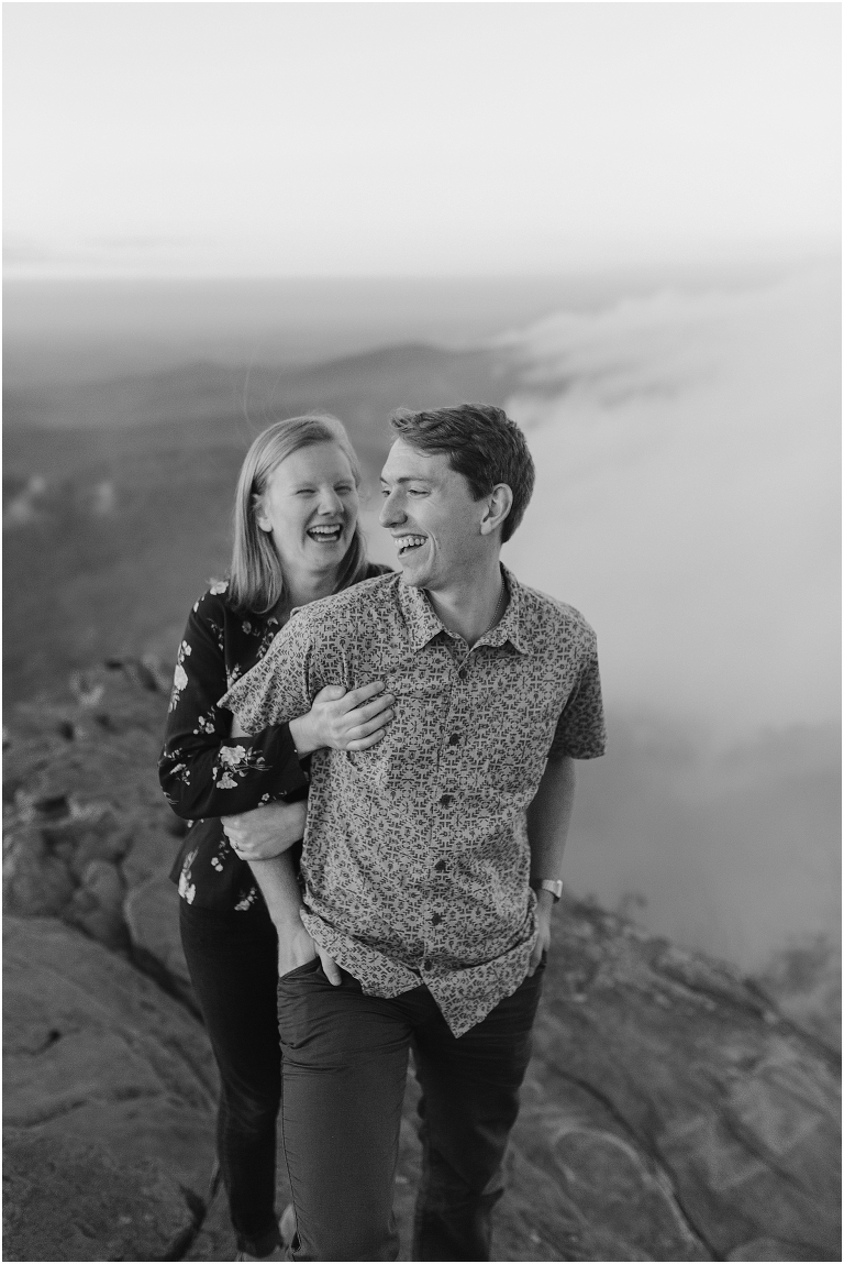 Couple sits together at Humpback Rocks during sunset, surrounded by fall colors and mountain fog.