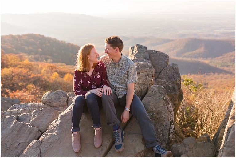 Couple sits together at Humpback Rocks during sunset, surrounded by fall colors and blue sky.