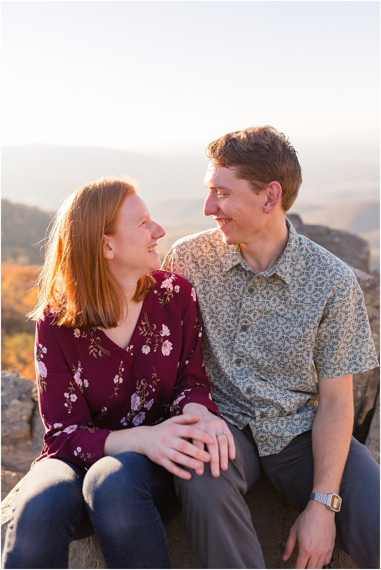 Couple sits together at Humpback Rocks during sunset, surrounded by fall colors and blue sky.
