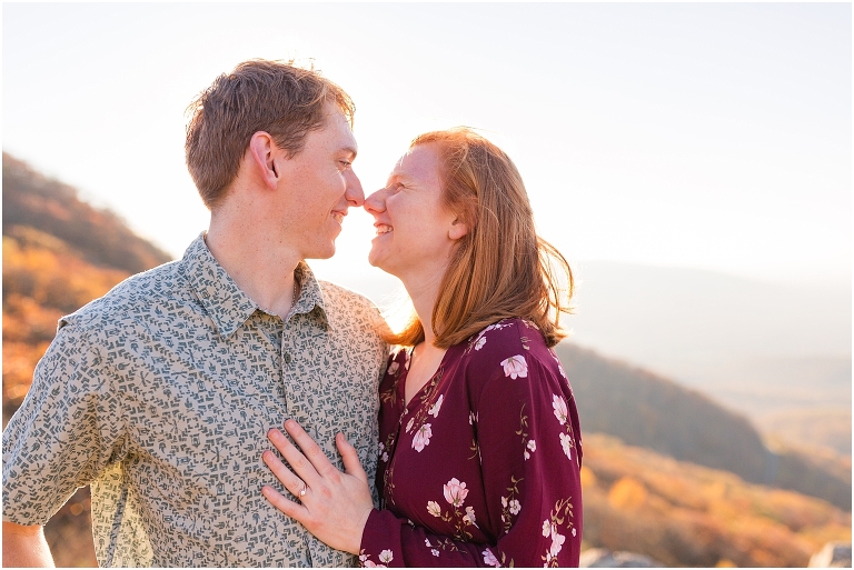 Couple sits together at Humpback Rocks during sunset, surrounded by fall colors and blue sky.