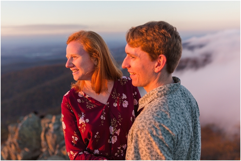 Couple at engagement session at Humpback Rocks during sunset, surrounded by fall colors, blue sky, and mountain fog.
