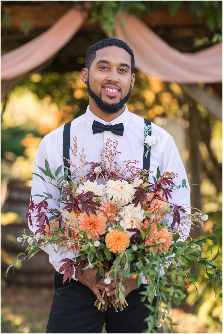 Autumn wedding inspiration color palette with groom in front of golden hour arbor holding bouquet