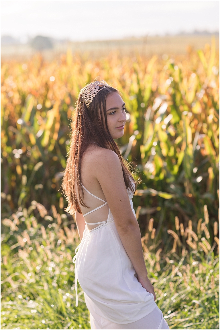 Demeter Greek Mythology goddess of agriculture inspired portrait session white dress golden crown in an open field next to corn with a sunrise mountain view