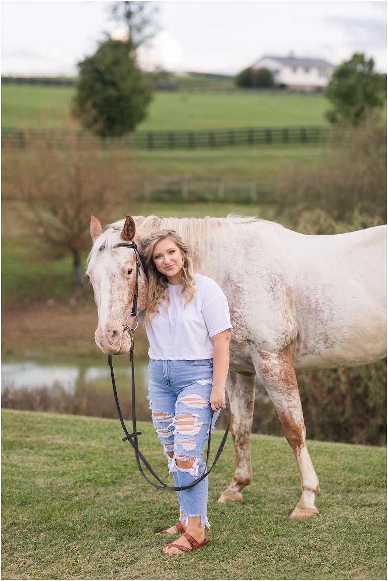 Senior horse portraits with a casual outfit white t-shirt blue jeans and a white and rust mare in an open field at a horse barn, Virginia senior graduation portrait photographer