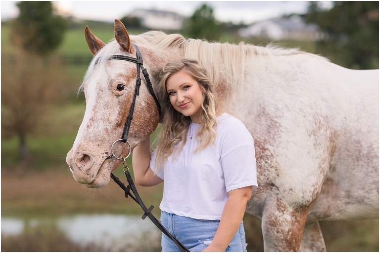 Senior horse portraits with a casual outfit white t-shirt blue jeans and a white and rust mare in an open field at a horse barn, Virginia senior graduation portrait photographer