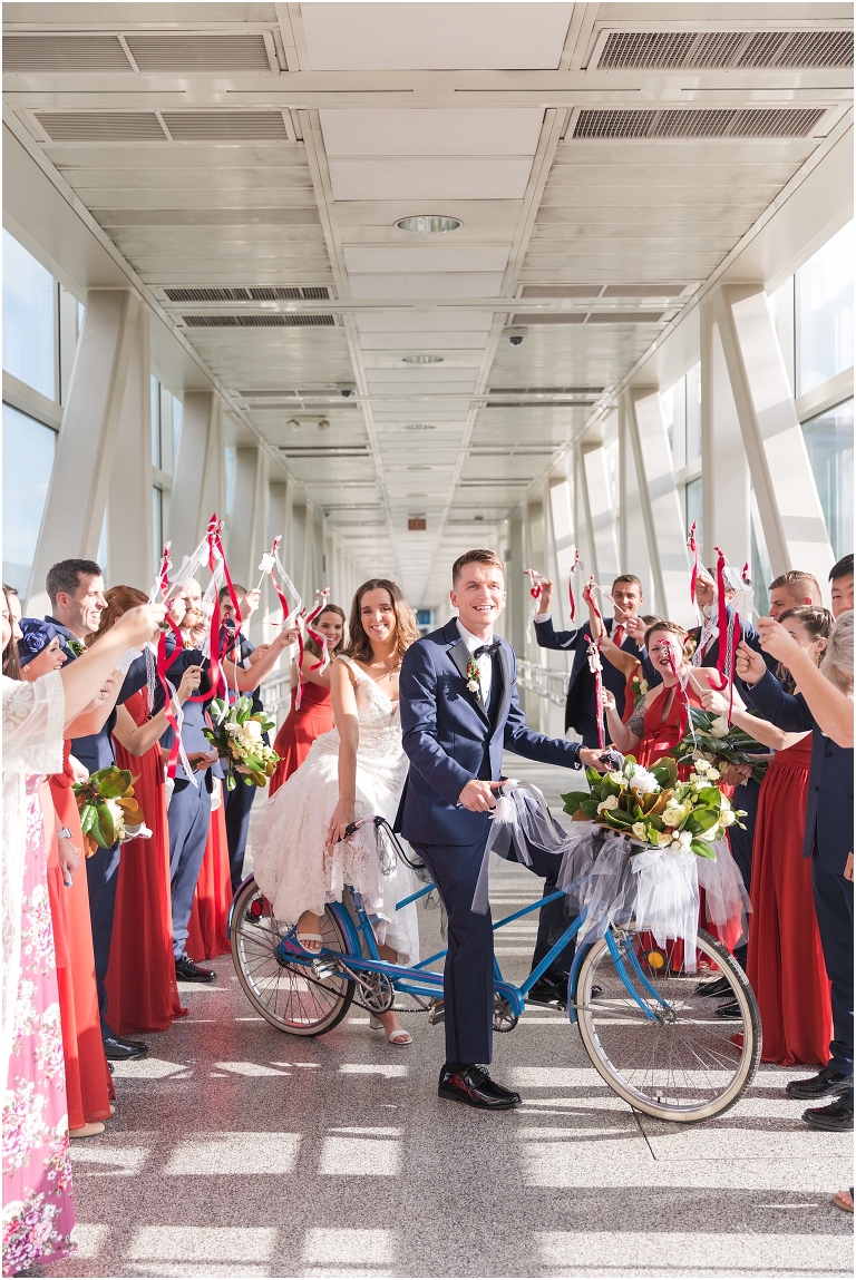 Savanna & Colin's Roanoke wedding with portraits under the magnolia trees at Hotel Roanoke and a reception and newlywed portraits at the Taubman Museum of Art. Wedding party exit photo with the newlyweds on a tandem bike