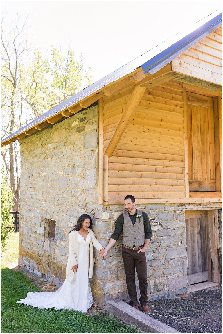 Family farm and barn spring wedding first touch between bride and groom around a brick and wood shed
