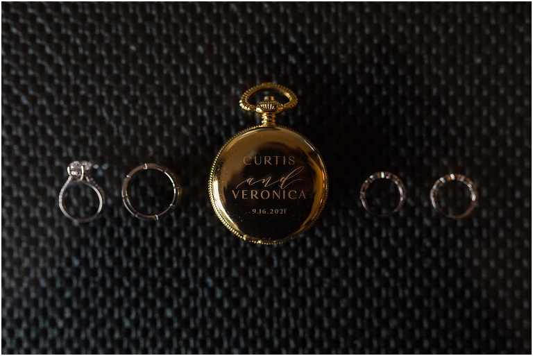 Rings surrounding a customized pocket watch with their names and wedding date engraved waiting for the couple to finish getting ready in their hotel rooms for their Virginia elopement