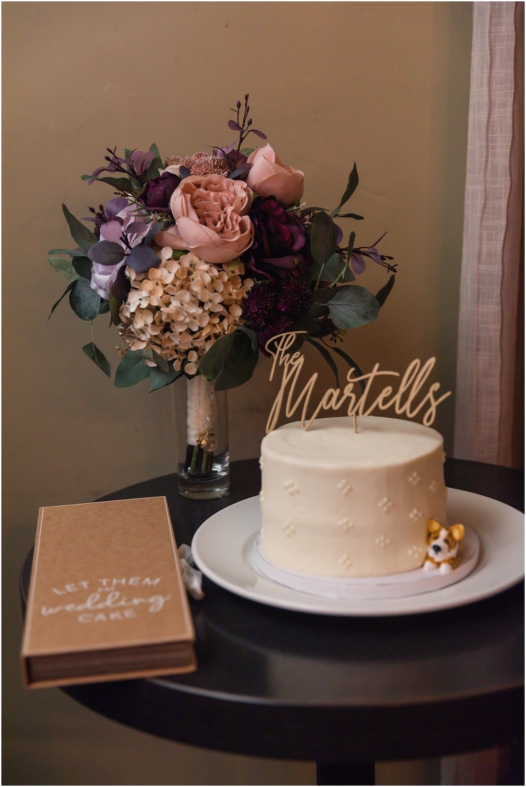 The reception setup at Tavola restaurant in Charlottesville, Virginia with their white cake with their last name cake topper and a molding of their dog, along with a cake cutting box that says Let Them Eat Wedding Cake